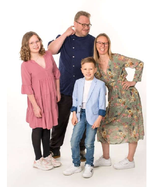 Eine Familie von vier Personen, bestehend aus einem Vater, einer Mutter und zwei Kindern, steht lächelnd nebeneinander.